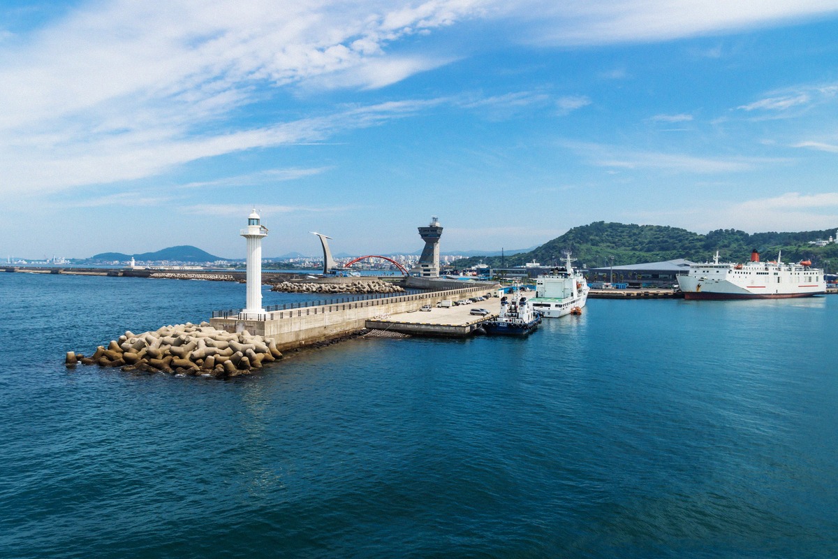 Ferry at the terminal in Jeju City port, seen from the sea past the white mole lighthouse