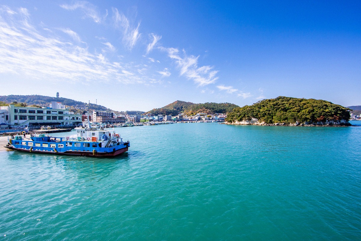 Blue and white car ferry at the Wando passenger terminal, with the wooded island of Judo in the harbour